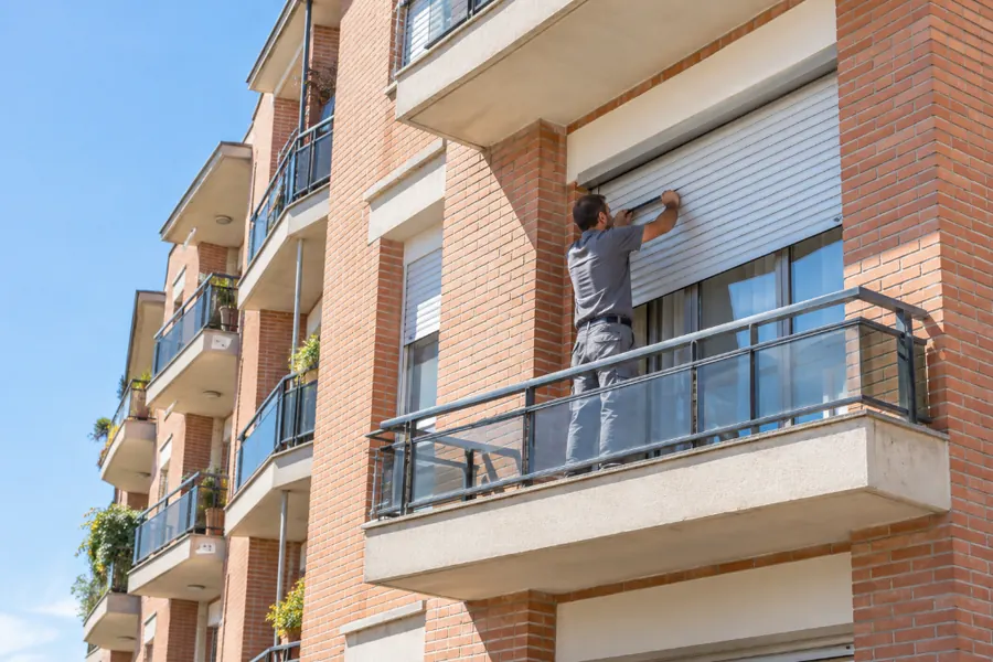 Persianista ajustando una persiana enrollable en el balcón de un bloque de pisos de ladrillo
